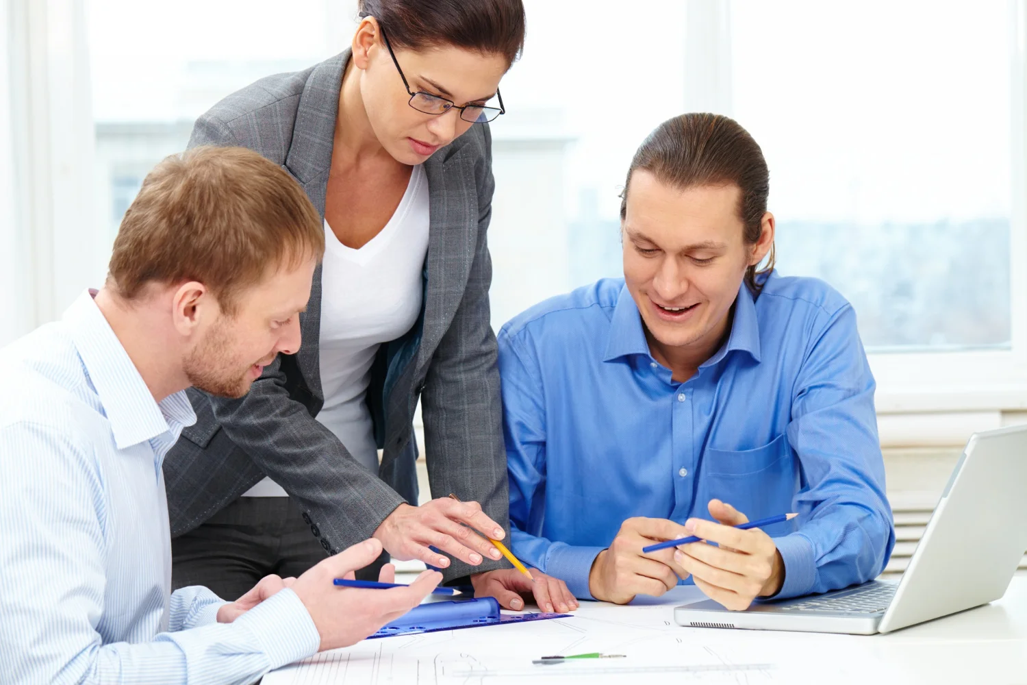 Three professionals engaged in a collaborative meeting, discussing plans and reviewing documents with a laptop on the table.