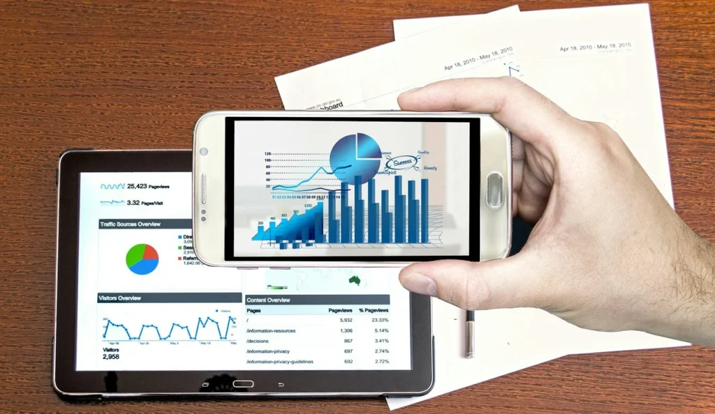 Hand holding a smartphone displaying a digital graph overlaid on tablet screens showing analytics and reports.