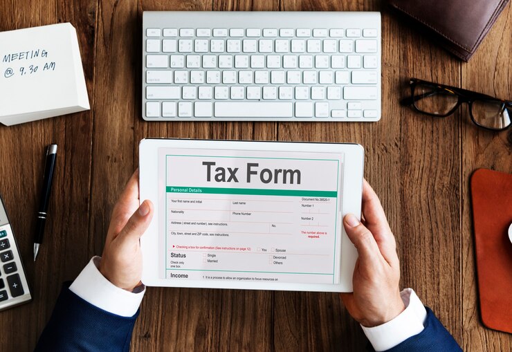 Individual holding a tax form on a tablet, showcasing personal details and income status, surrounded by office supplies.